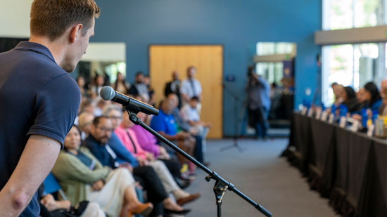 Man speaking into a microphone in a large room full of people