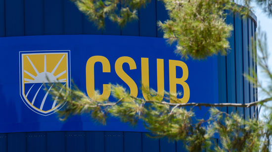 CSUB logo on a blue tower with tree branches in foreground